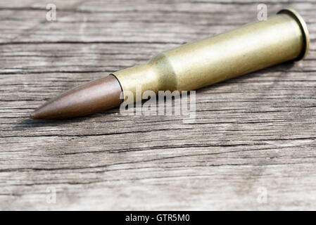 Unico crudi 7,62 mm bullet e ottone carcassa diagonale giacente su un età compresa tra una superficie di legno. Copia area spazio per militari o guntradi Foto Stock