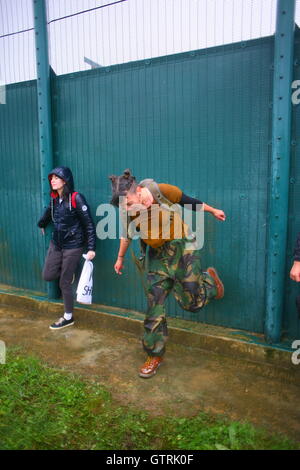 Milton Ernest, Bedford, Regno Unito. 10 settembre 2016. Un uomo vestito con tonalità camouflage e marroni si bilancia su un piede mentre sfreccia in una recinzione di sicurezza, mentre un compagno di colore nero porta con sé una borsa della spesa contrassegnata con "SH". Centinaia di manifestanti protestano contro il recinto del centro di detenzione Yarls Wood chiedendo la chiusura della struttura. Penelope Barritt/Alamy Live News Foto Stock