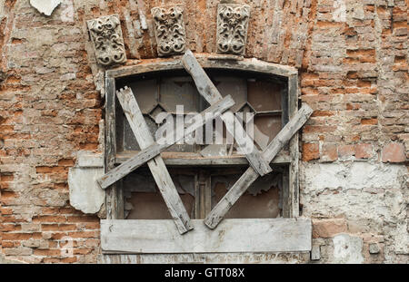 Vista frontale di una finestra danneggiati coperti con tavole di legno Foto Stock