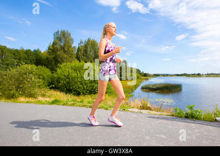 Sporty giovane donna corre su strada lungo l'acqua Foto Stock