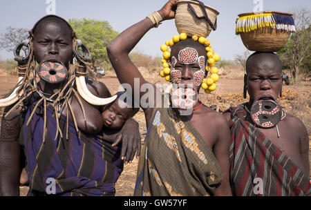 Tre donne Mursi della valle dell'Omo in Etiopia con labbro di piastre ossee, orecchini, copricapo e corpo rituale vernice, uno con il bambino Foto Stock