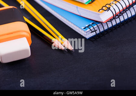 Forniture scolastiche matita, eraser, notebook su uno sfondo scuro Foto Stock