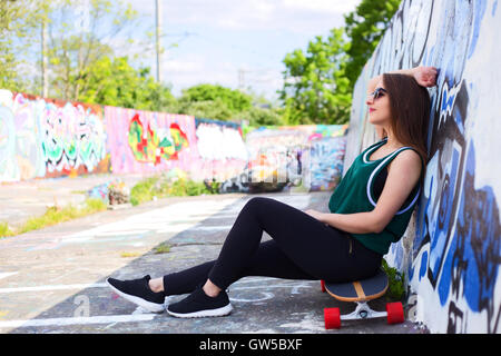 Giovane donna seduta su uno skateboard in un skate park Foto Stock