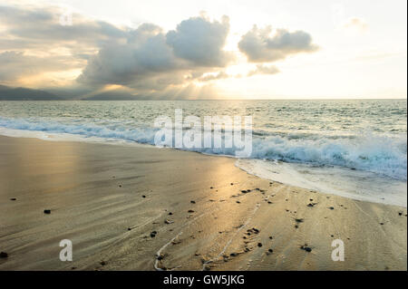 Ocean raggi del sole è un luminoso edificante seascape con raggi di sole rottura attraverso le nuvole come un onda dolce rotoli a riva. Foto Stock