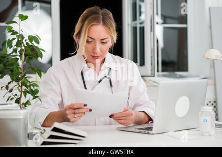 Metà femmina adulta del medico la lettura dei documenti in ufficio Foto Stock