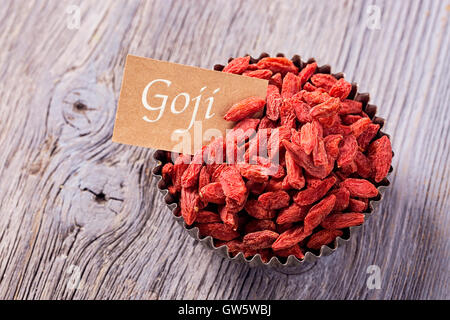 Bacche di Goji in una ciotola su uno sfondo di legno Foto Stock