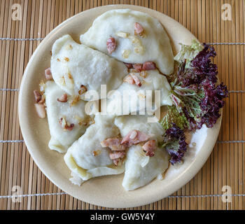 Tradizionale polacco Pierogi gnocchi ripieni servita su un piatto di terracotta e decorate con prosciutto e cipolla fritti Foto Stock