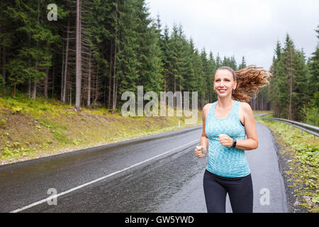 Giovane donna slim jogging sulla strada di montagna a piovosa mattinata Foto Stock