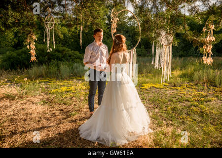 Sposa e lo sposo in posa vicino il fascino in una struttura ad albero nella foresta. Accessori per matrimonio sull'albero. Accessori Hippie sulla struttura ad albero Foto Stock