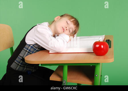 Ragazza in uniforme scolastica a dormire la sua scrivania isolato su sfondo verde Foto Stock