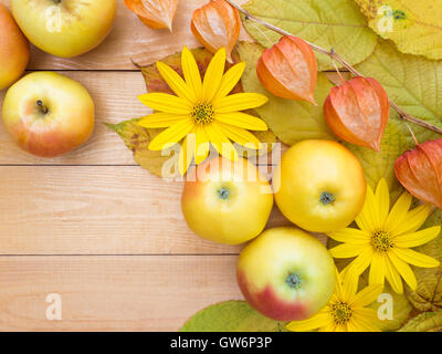 Mele, fiori gialli, physalis lanterne e foglie di autunno su tavole di legno sfondo Foto Stock