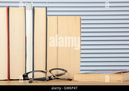 Logoro la lettura di libri in posizione verticale su un tavolo con degli occhiali in posa davanti a loro Foto Stock