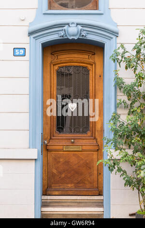 Vista su una porta di legno con un piccolo cuore di argento come decorazione. Color crema, parete blu il telaio della porta e il numero civico 59. Foto Stock