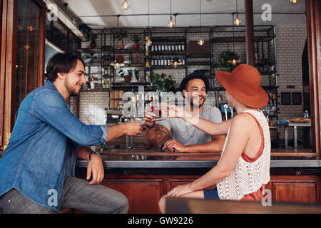 Giovani amici presso il cafe tostare un drink seduti ad un tavolo. Tre giovani, due uomini e una donna incontro in un coffee shop Foto Stock