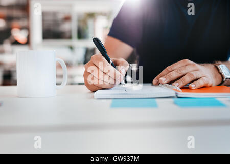 Ritagliato shot dell uomo la scrittura sul blocco note. La mano di imprenditore a prendere appunti mentre è seduto alla sua scrivania in ufficio. Foto Stock