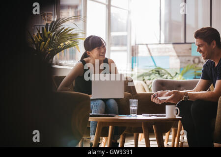 Colpo di due partner commerciali seduti nella hall di office e sorridente. Donna con notebook discutere idee di business con colleag maschio Foto Stock
