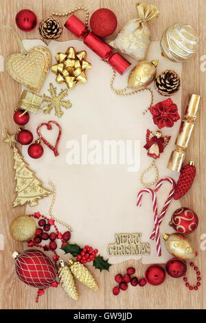 Rosso e oro sullo sfondo di Natale confine con addobbi per l'albero e baubles oltre il rovere chiaro sfondo su carta pergamena. Foto Stock