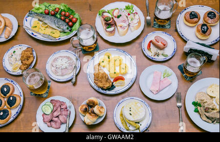 Il cibo dal di sopra su un tavolo di legno con i giovani intorno a mangiare una grande varietà di cibi Foto Stock