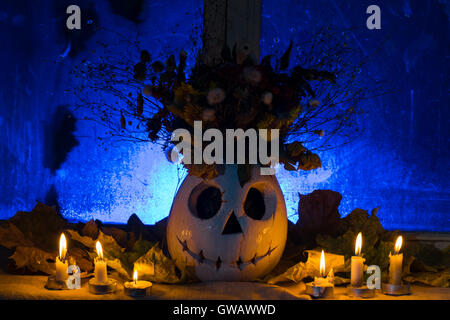 Foto di zucca di un vaso con fiori per una vacanza di Halloween. Il vaso costi di zucca contro una vecchia finestra, foglie secche di un Foto Stock