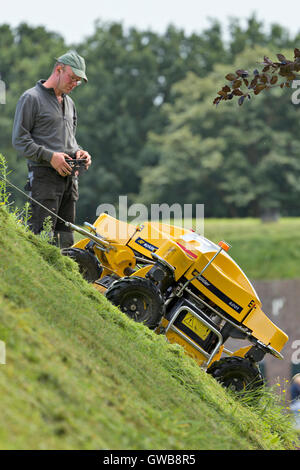 Un controllo remoto industriale taglierina di erba su una pendenza ripida parete della città della città di Naarden vesting. Foto Stock