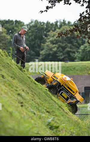 Un controllo remoto industriale taglierina di erba su una pendenza ripida parete della città della città di Naarden vesting. Foto Stock