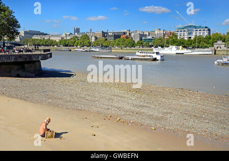 Londra, Inghilterra, Regno Unito. Il fiume Tamigi con la bassa marea. L uomo a prendere il sole con la sua maglietta off, vicino alla Tate Modern sulla banca del sud Foto Stock