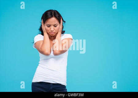 Bellissima giovane donna vietnamita che copre le sue orecchie con palme su sfondo blu Foto Stock