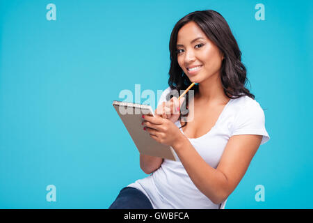 Considerato giovane donna vietnamita pensando a qualcosa e notebook di contenimento isolato su uno sfondo blu Foto Stock