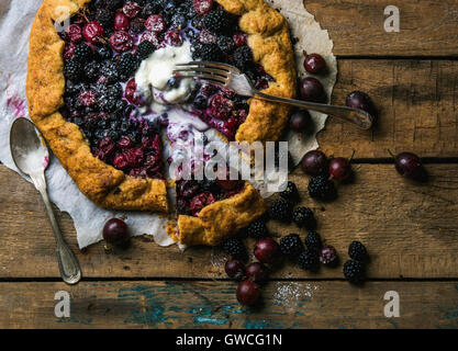 In casa giardino berry galetta o crostata Torta dolce con fuso con gelato alla vaniglia scoop su legno rustico sfondo. Vista superiore, h Foto Stock