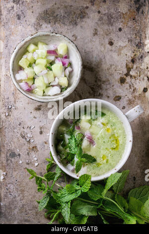 Tazza di ceramica di cetriolo gazpacho zuppa fredda con la menta, cipolla, olio d'oliva e servite con ingredienti su ferro vecchio sfondo con Foto Stock