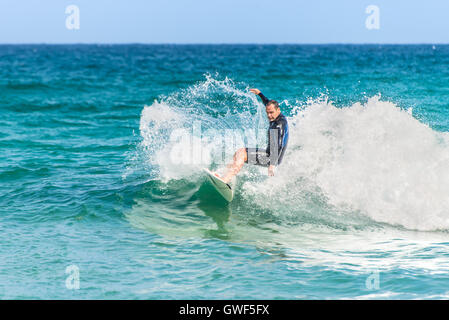 Un uomo che cavalca il suo surfboard verso la riva. Foto Stock