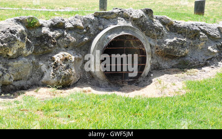 Canale sotterraneo roccioso con il tubo rivestito con metallo arrugginito grata in fossa con erba verde da carreggiata in Western Australia. Foto Stock