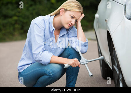 Frustrati Driver femmina con ferro di pneumatico cercando di cambiare la ruota Foto Stock