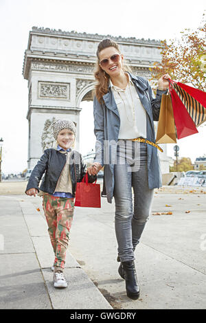 Elegante autunno a Parigi. A piena lunghezza Ritratto di giovane sorridente madre e figlia con borse per lo shopping nelle vicinanze del Arc de Triomphe a Parigi, Francia andando avanti Foto Stock