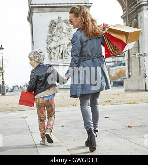 Elegante autunno a Parigi. Visto da dietro a piena lunghezza Ritratto di felice giovane madre con bambino e borse per lo shopping in Parigi, Francia cercando riposo e passeggiate Foto Stock
