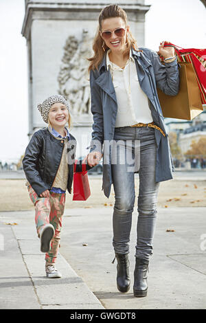 Elegante autunno a Parigi. A piena lunghezza Ritratto di giovane sorridente madre con bambino e borse per lo shopping nelle vicinanze del Arc de Triomphe a Parigi, Francia andando avanti Foto Stock