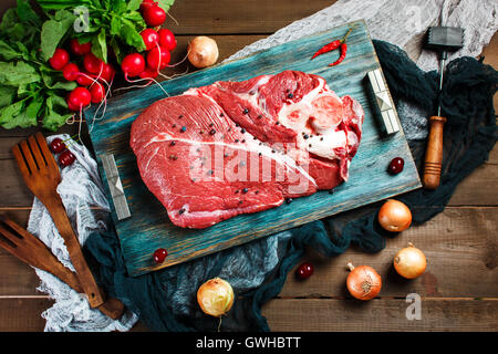 Carni fresche bovine Carne di vitello su tavola in legno rustico con utensili da cucina e verdure, vista dall'alto Foto Stock