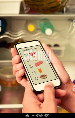 Giovane uomo che fa la sua lista nel suo smartphone, con immagini di diversi prodotti di colpo da me stesso nella sua schermata, nella parte anteriore Foto Stock
