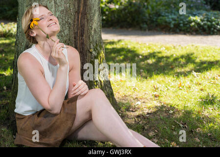 Bella donna bionda è seduto vicino a un albero e sognare Foto Stock