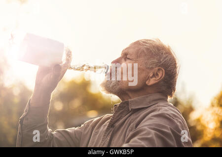 Il senior beve l'acqua dalla bottiglia Foto Stock
