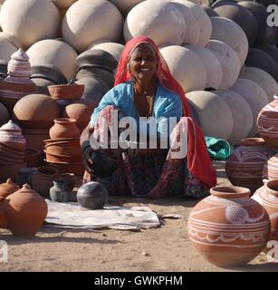 Un sorridente donna indiana in tipici abiti e gioielli del Rajasthan, NW India siede sulla terra la vendita di argilla rotondo vasi d'acqua Foto Stock
