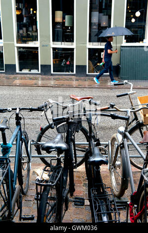 Uomo che cammina sotto la pioggia accanto ad un bike park, Copenhagen, Danimarca Foto Stock