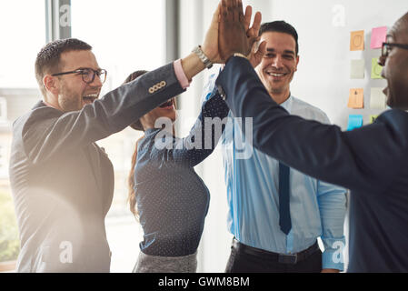 Felice successo multirazziale team aziendali fornendo un alto cinque gesto come ridono e allietare il loro successo Foto Stock