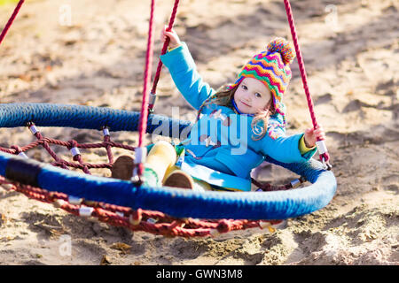 Bambina in caldo cappotto e hat su un parco giochi. Bambino che gioca all'aperto in autunno. Bambini giocano sul cortile della scuola Foto Stock