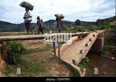 Tre persone sono a piedi su un piccolo ponte di legno fatto di alcune linee che ha sostituito un crollato ponte di cemento ( Madagascar) Foto Stock