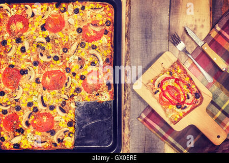 Vintage nei toni del tonno in casa la pizza con pomodori, olive, cipolla e mais su sfondo di legno, vista dall'alto. Foto Stock