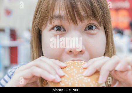 La bellezza della donna in cafe mangiare hamburger Foto Stock