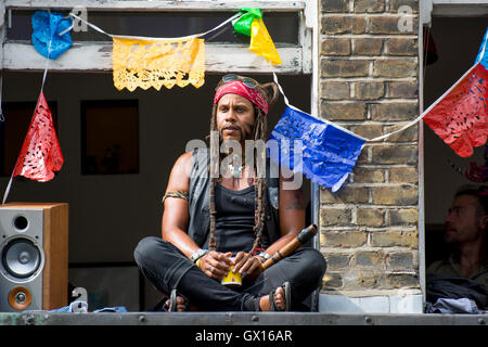 Persone in windows durante il cinquantesimo carnevale di Notting Hill celebrazioni; finestre decorate con ghirlande colorate Foto Stock