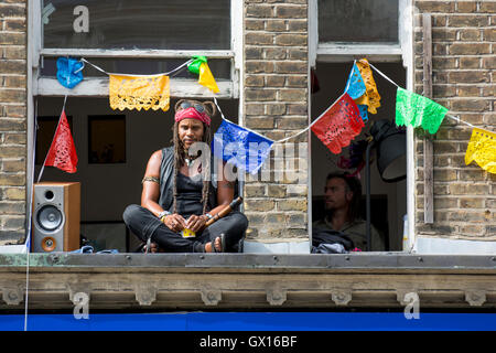 Persone in windows durante il cinquantesimo carnevale di Notting Hill celebrazioni; finestre decorate con ghirlande colorate Foto Stock