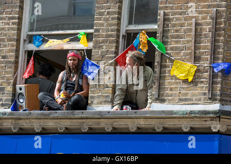 Persone in windows durante il cinquantesimo carnevale di Notting Hill celebrazioni; finestre decorate con ghirlande colorate Foto Stock